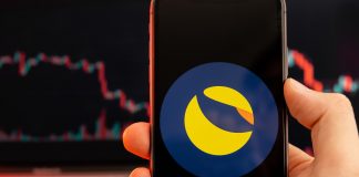 Terra LUNA cryptocurrency logo on the screen of smartphone in mans hand with downtrend on the chart on a red light background, February 2022, San Francisco, USA.