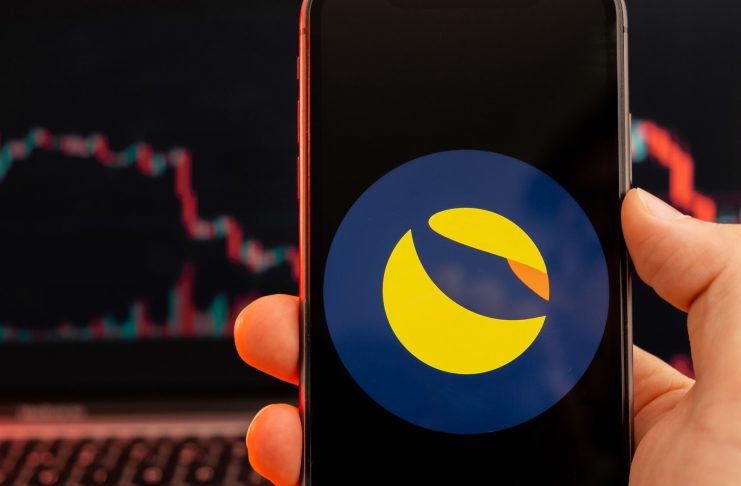 Terra LUNA cryptocurrency logo on the screen of smartphone in mans hand with downtrend on the chart on a red light background, February 2022, San Francisco, USA.